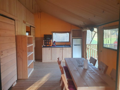 Intérieur d'une tente safari avec cuisine, table et chaises au Moulin du Pommier Glamping & Camping en France.