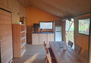 Interior of a safari tent with kitchen, dining table, and chairs at Moulin du Pommier Glamping & Camping in France.