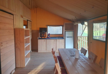 Interior de una tienda safari con cocina, mesa y sillas en Moulin du Pommier Glamping & Camping en Francia.