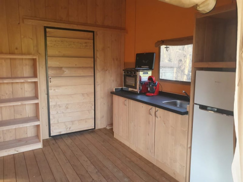 Interior de tienda safari con cocina, estantes, mini horno y nevera en Moulin du Pommier Glamping & Camping.