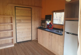 Interior de tienda safari con cocina, estantes, mini horno y nevera en Moulin du Pommier Glamping & Camping.