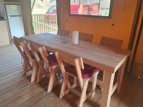 Interior view of dining area in safari tent featuring wooden table and six chairs at Moulin du Pommier in France.