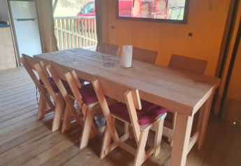 Vista interna dell'area pranzo in tenda safari con tavolo in legno e sei sedie a Moulin du Pommier in Francia.