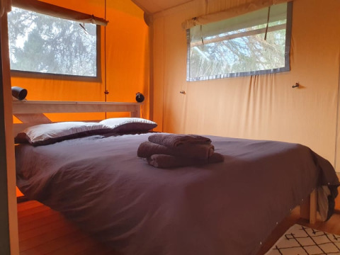 Dormitorio en tienda safari con cama doble, toallas y ventanas en Moulin du Pommier Glamping & Camping en Francia.