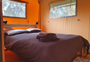Dormitorio en tienda safari con cama doble, toallas y ventanas en Moulin du Pommier Glamping & Camping en Francia.