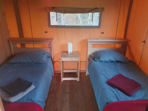 Due letti singoli con biancheria blu in una tenda safari al Moulin du Pommier Glamping & Camping in Francia.