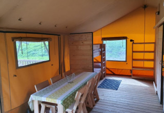 Binnenaanzicht van een safaritent met eettafel, stoelen, stapelbed en planken bij Moulin du Pommier Camping.