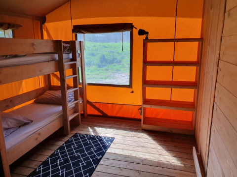 Interior de tienda safari con literas, estanterías y ventana en Moulin du Pommier Glamping & Camping en Francia.