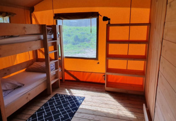 Interno di tenda safari con letti a castello, scaffali e finestra al Moulin du Pommier Glamping & Camping in Francia.
