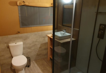 Bathroom in a safari tent featuring toilet, shower, and sink at Moulin du Pommier Glamping & Camping in France.
