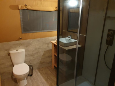Salle de bain dans une tente safari avec toilettes, douche et lavabo au Moulin du Pommier Glamping & Camping en France.