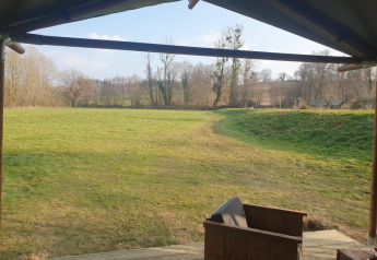 View from a safari tent at Moulin du Pommier Glamping & Camping in France looking over grass field and trees.