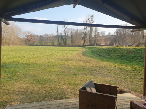 View from a safari tent at Moulin du Pommier Glamping & Camping in France looking over grass field and trees.