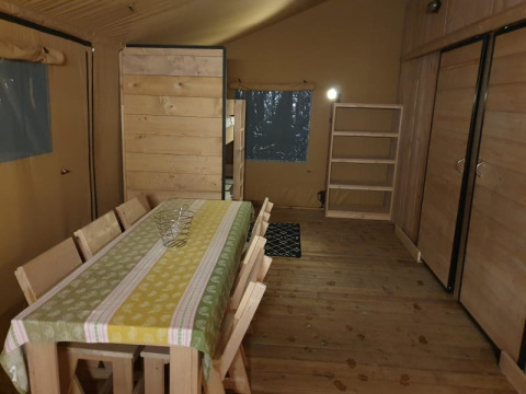 Interior de una tienda safari con mesa, sillas y estantería en Moulin du Pommier Glamping en Francia.