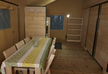 Interior de una tienda safari con mesa, sillas y estantería en Moulin du Pommier Glamping en Francia.