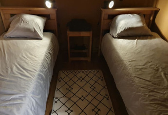 Due letti singoli con lenzuola bianche, cuscini, un tavolino e tappeto su pavimento in legno in tenda safari.
