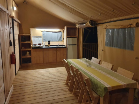 Indretning af safari telt med træbord, stole, køkken og køleskab hos Moulin du Pommier Glamping i Frankrig.