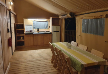 Indretning af safari telt med træbord, stole, køkken og køleskab hos Moulin du Pommier Glamping i Frankrig.
