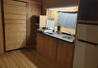 Kitchen area inside a safari tent with wood paneling, stove, sink, and fridge at Moulin du Pommier Glamping & Camping.
