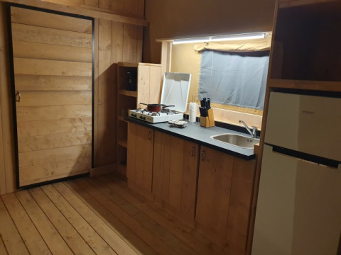 Kitchen area inside a safari tent with wood paneling, stove, sink, and fridge at Moulin du Pommier Glamping & Camping.