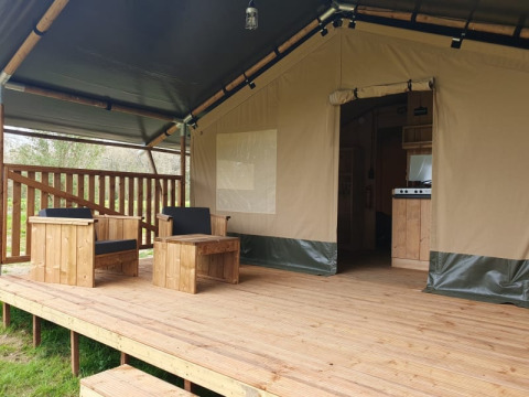 Tienda safari con terraza de madera y asientos al aire libre en Moulin du Pommier Glamping & Camping, Francia.