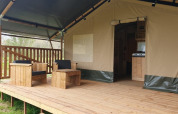 Tenda safari con veranda in legno e sedute presso Moulin du Pommier Glamping & Camping in Francia.