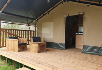 Tienda safari con terraza de madera y asientos al aire libre en Moulin du Pommier Glamping & Camping, Francia.
