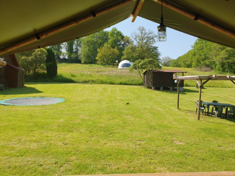 View from safari tent overlooking green lawn, sunken trampoline, wooden shed, and dome tent in distance.