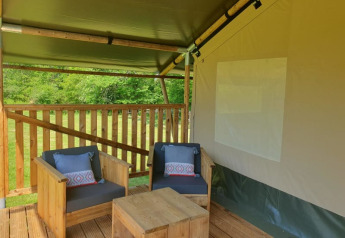 Outdoor lounge with wooden furniture inside a safari tent at Moulin du Pommier Glamping & Camping, France.