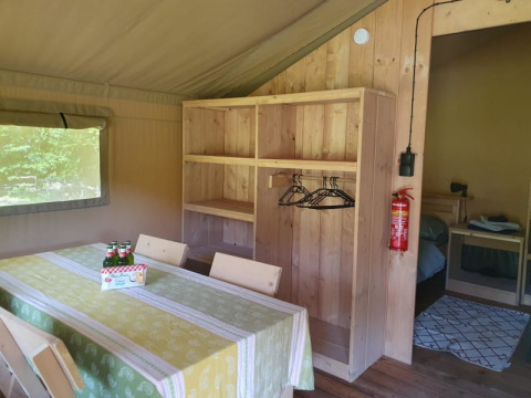 Interior de tienda safari con mesa de comedor, sillas, estanterías y dormitorio en Moulin du Pommier Glamping & Camping en Francia.