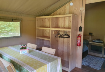 Interior de tienda safari con mesa de comedor, sillas, estanterías y dormitorio en Moulin du Pommier Glamping & Camping en Francia.