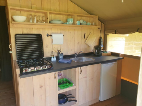 Cocina equipada en tienda safari con estufa, fregadero y nevera en Moulin du Pommier Glamping, Francia.