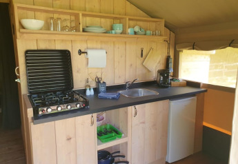 Well-equipped kitchen inside a safari tent with stove, sink, fridge and dishes at a French glampsite.