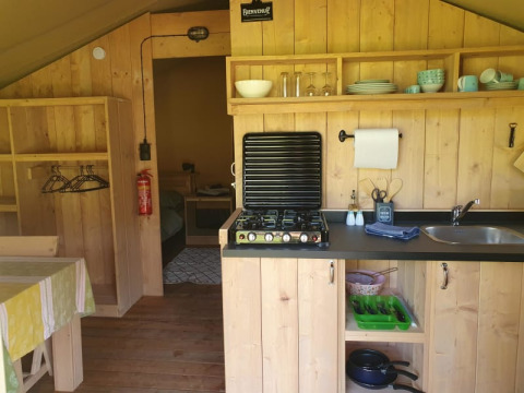 Zona de cocina en una tienda safari con estufa de gas, fregadero y estanterías en Moulin du Pommier Glamping & Camping.