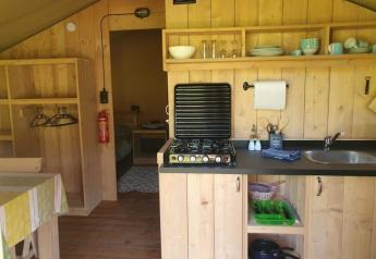 Zona de cocina en una tienda safari con estufa de gas, fregadero y estanterías en Moulin du Pommier Glamping & Camping.