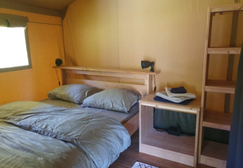 Safari tent interior at Moulin du Pommier Glamping & Camping, France, with double bed, wooden shelves and lamp.