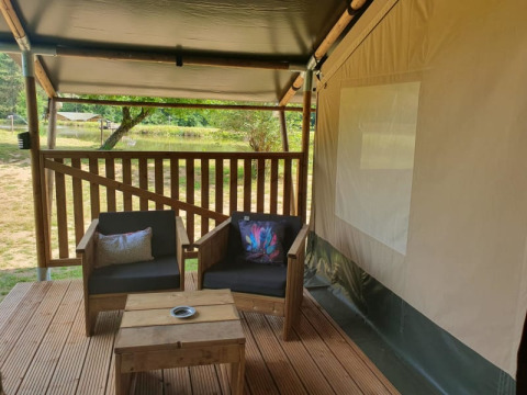 Terraza de madera con sillones frente a una tienda safari en Moulin du Pommier Glamping & Camping, Francia.