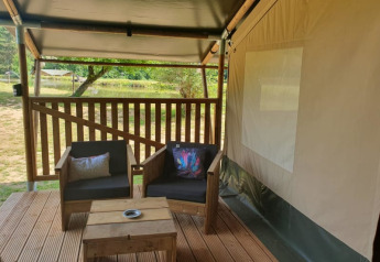 Terraza de madera con sillones frente a una tienda safari en Moulin du Pommier Glamping & Camping, Francia.
