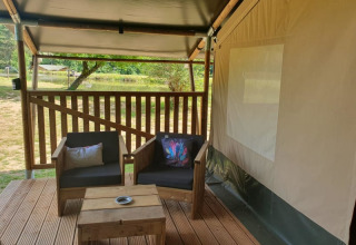 Terraza de madera con sillones frente a una tienda safari en Moulin du Pommier Glamping & Camping, Francia.