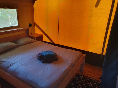 Interior de dormitorio en tienda safari con cama doble, ventana y toallas en Moulin du Pommier en Francia.