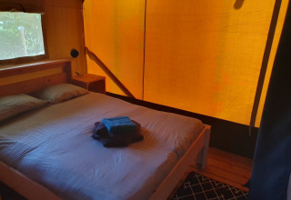 Interior de dormitorio en tienda safari con cama doble, ventana y toallas en Moulin du Pommier en Francia.