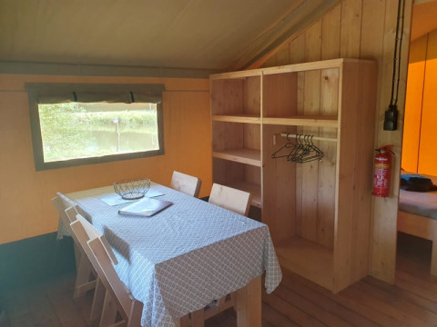 Interior de una tienda safari con mesa de comedor, sillas y estantería en Moulin du Pommier Glamping & Camping, Francia.