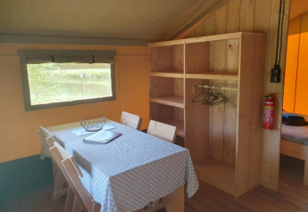 Interno di una tenda safari con tavolo da pranzo, sedie e scaffali al Moulin du Pommier Glamping & Camping in Francia.