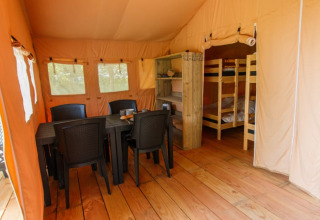 Interior de una tienda safari con suelo de madera, mesa de comedor, sillas negras y literas en la zona de dormir.
