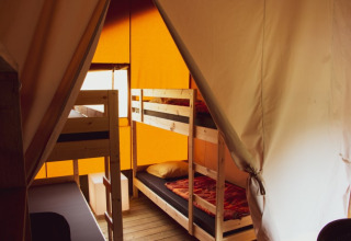 Intérieur d'une tente safari avec lits superposés en bois, ambiance chaleureuse et lumière orangée.