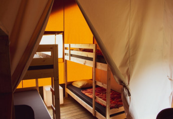 Innenansicht eines Safarizelts mit Etagenbetten und Holzboden, beleuchtet durch orange Zeltwände.