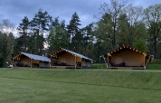 Safari tents with string lights at Camping Sonnenberg in Germany, set among trees and green lawn at dusk.