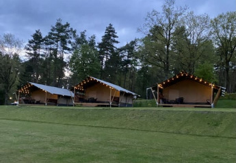 Safari tents with string lights at Camping Sonnenberg in Germany, set among trees and green lawn at dusk.