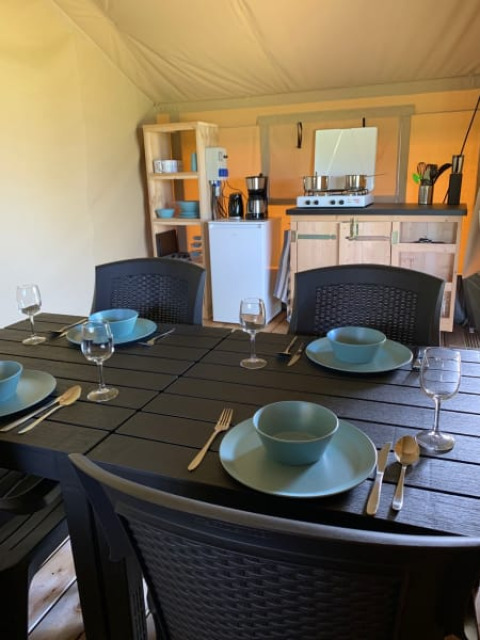 Dining area and kitchen inside safari tent at Camping Sonnenberg, Germany, table set for four people.