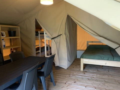 Interior of a safari tent at Camping Sonnenberg in Germany, featuring a dining table, bunk beds, and a double bed.